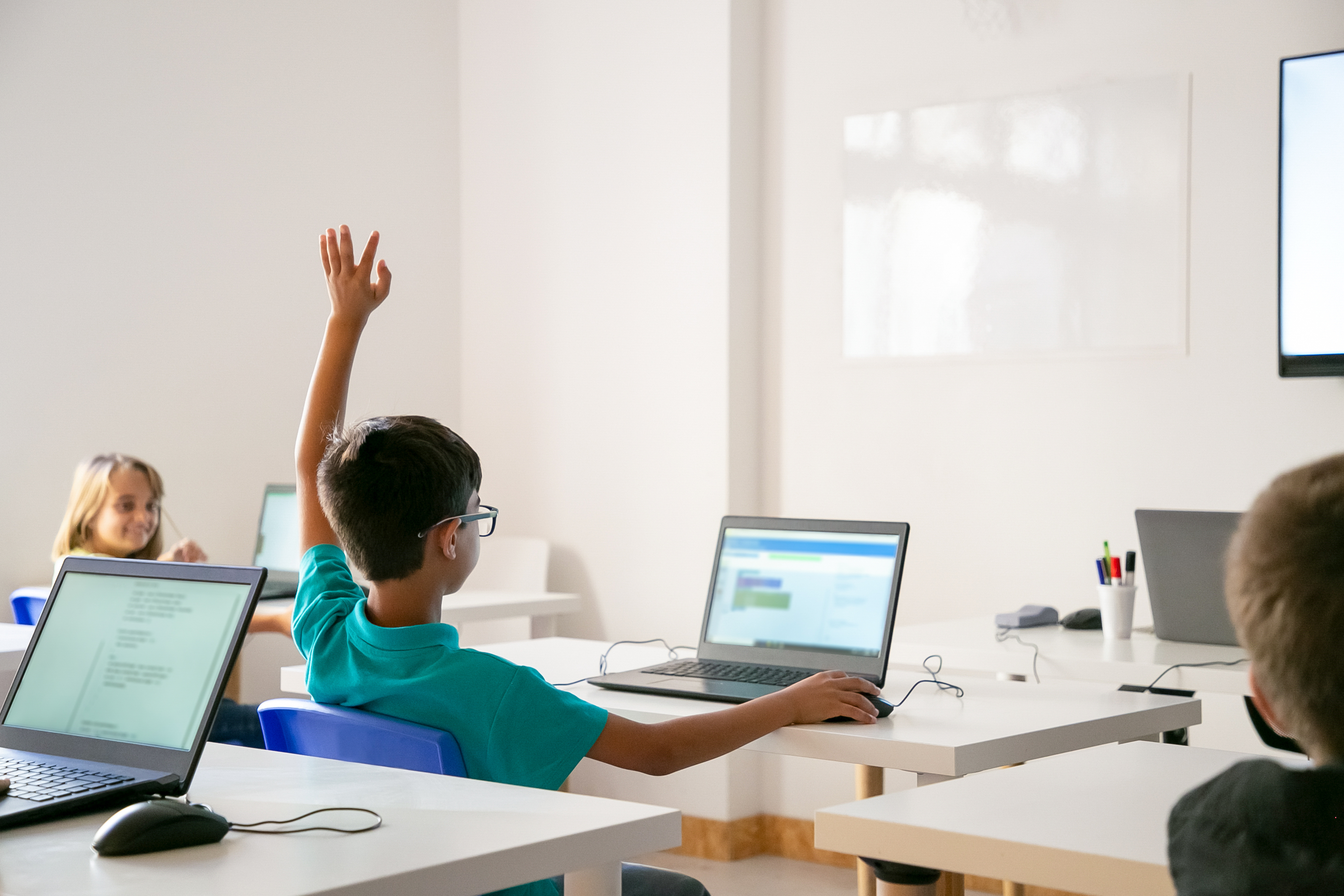 This is an image of a little boy in a classroom raising his hand.